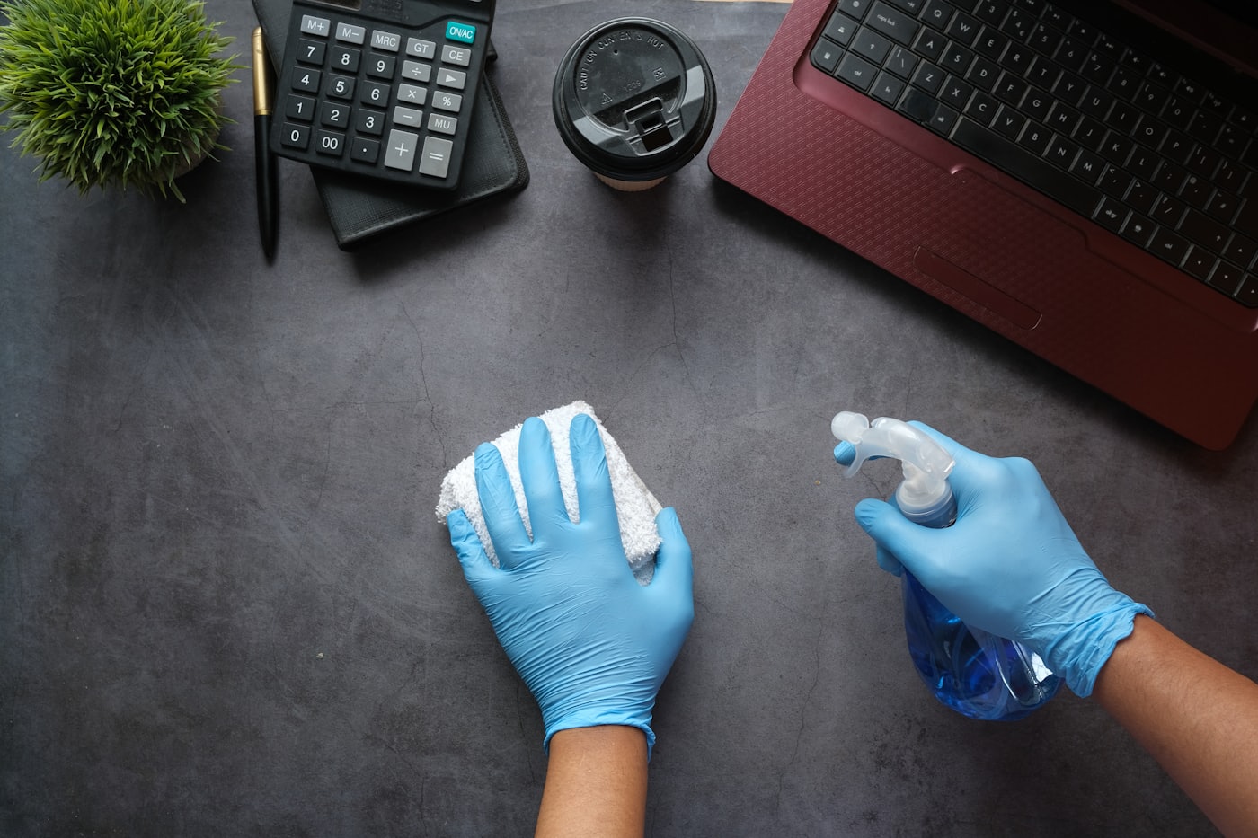 Manos con guantes limpiando un escritorio con rociador y paño, aseo de oficinas en Chile